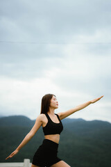 Obraz premium A woman standing outdoors with eyes closed, breathing deeply and stretching her arms, embracing calmness and nature.