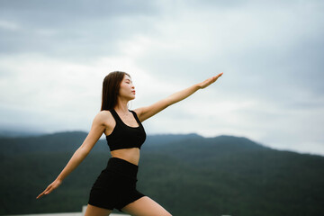 Obraz premium A woman standing outdoors with eyes closed, breathing deeply and stretching her arms, embracing calmness and nature.