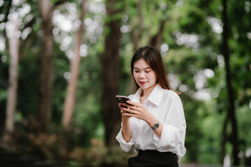 Business woman sitting outdoors smiling while using smartphone, working or chatting in modern city environment with blurred background lights.