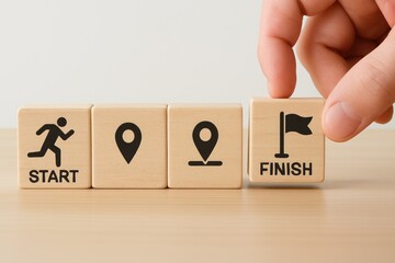 Hand arranges wooden blocks with start and finish icons and location markers for a journey path progress