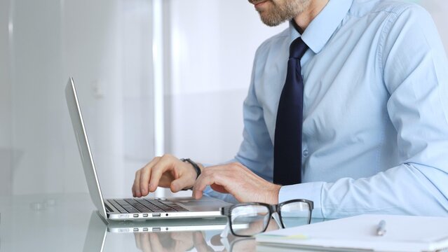 Businessman working on laptop in modern office, typing on keyboard and concentrating on corporate projects. Business and technology conceptal corporate tasks. Business people concept