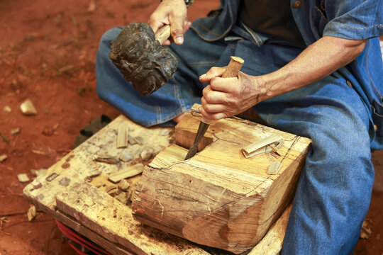 Focused craftsman carving wood block with traditional hammer and chisel. woodworking artist shows great skill and precision in rustic workshop, concentrating on manual labor