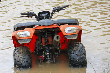 Powerful orange all terrain vehicle stuck in deep muddy flood water after storm. abandoned quad faces challenging problem, submerged in dirty, murky river © CoreRock