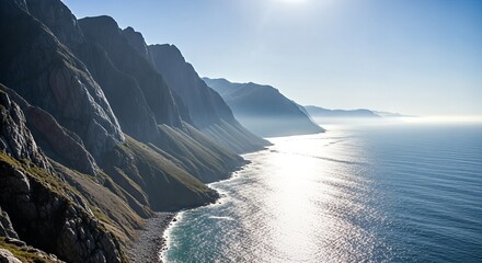 Sunlight glints off the ocean as waves crash against the rugged, steep cliffs of a coastal mountain range.