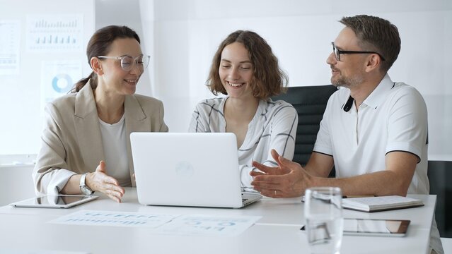 Professional team reviewing project data on laptop, working together in modern office environment, collaborating with focused corporate energy. Business people concept