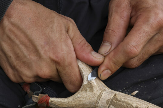 Close up view of focused hands carving wood with sharp knife. This skilled artisan works on traditional craft, whittling small sculpture with intense concentration