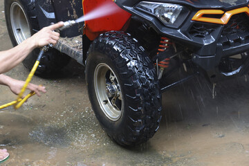 Man washing muddy red off road vehicle with water hose, showing satisfaction of cleaning after an...