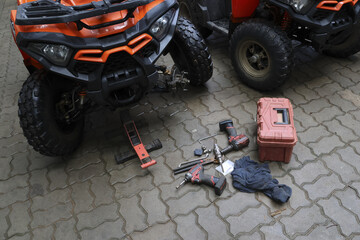 Orange ATV quad bike on paved ground with tools for repair and maintenance. red toolbox and power drills ready for fixing off road vehicle before an adventure © CoreRock
