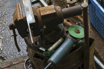 Close up of an old rusty vise and grinder power tool in cluttered workshop. This industrial equipment for metal work represents authentic craft, labor and industry