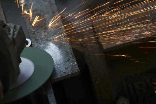 Focused worker at workshop using grinder tool on metal. industrial manufacturing process creates bright hot sparks from steel piece during manual work