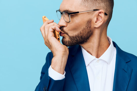 A professional businessman speaks on a mobile phone against a solid blue background, showcasing focused confidence, strong concentration, and calm determination in a contemporary setting.