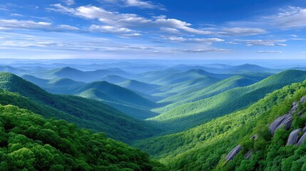Fototapeta premium Vast rolling green hills and distant blue mountains under a bright sunny sky with scattered white clouds, bathed in natural light and shadow.