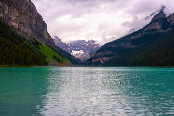 Scenic view of Lake Louise surrounded by mountains and evergreen trees in Banff, Canada during a cloudy day
