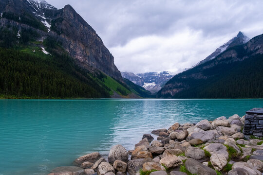 Scenic view of Lake Louise surrounded by mountains and evergreen trees in Banff, Canada during a cloudy day