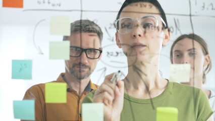 Professional team strategizing, writing collaborative notes on glass board, mapping innovative project workflow with marker © volha_r