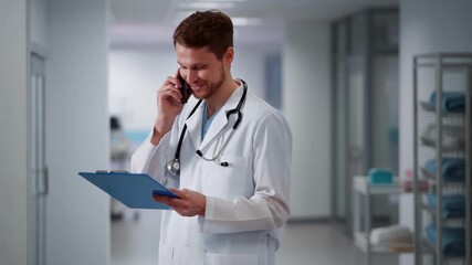 A doctor confidently consults on the phone while reviewing medical records in a bright hallway Stock Video - Powered by Adobe