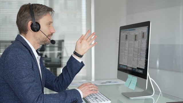 Man in headset talking during online video call, working in office, consulting remote customers, providing technical support. Business people concept