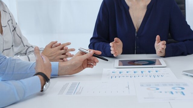 Professional colleagues examining financial documents, studying performance charts on paper and digital tablet during collaborative meeting in modern workplace setting