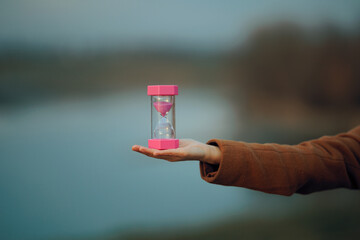 Hand of a Woman Holding an Hourglass Outdoors in Nature. Person with sand glass measuring time passing in a symbolic way
