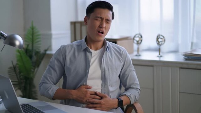A man experiencing stomach pain while working at his desk Stock Video