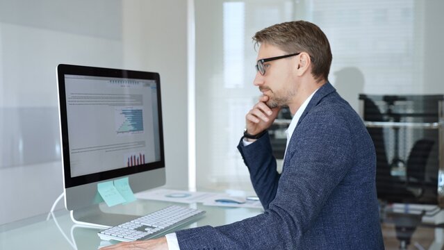 Businessman in a blue jacket analyzing financial data on computer, working in modern office, managing business strategy and reporting. Business people concept