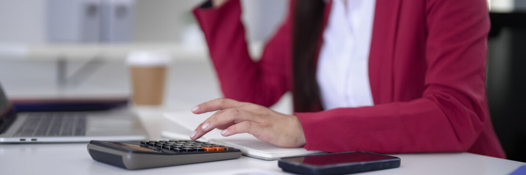 Adult Asian hand operates calculator performing financial computations for business professional tasks in modern office environment