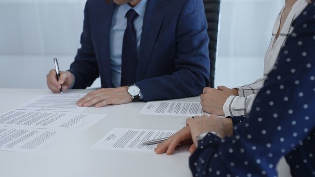 Professional businessman wearing tailored suit signing contract at sleek desk, sealing business agreement with collaborative partners in contemporary workspace