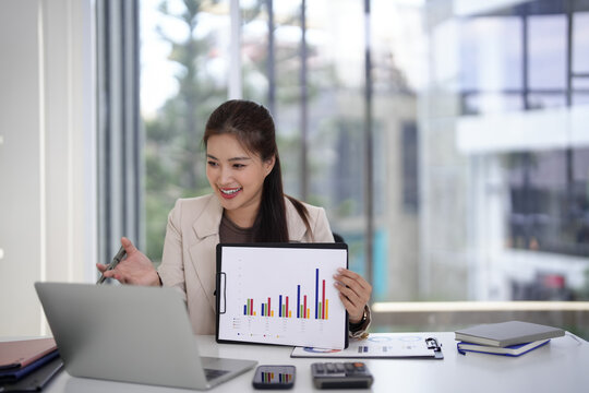 Asian adult woman business professional presents data analysis report showing growth in modern office workspace using laptop for strategy meeting - Powered by Adobe