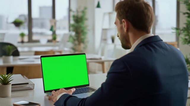 A businessman looking at a laptop with a green screen in a modern office. He is likely working on a project or video conference Stock Video