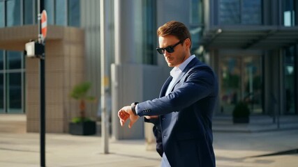 A businessman wearing a suit and sunglasses, checking his watch in front of a modern building. He appears to be waiting and checking time Stock Video - Powered by Adobe