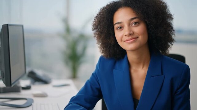 Confident businesswoman smiling while working at her desk. She is wearing a blue blazer and looking directly at the camera. Stock Video