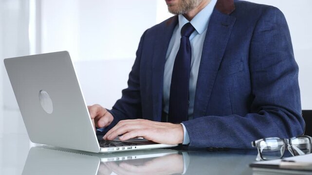 Professional businessman working on laptop computer, typing on keyboard in modern office, managing business tasks. Business people concept