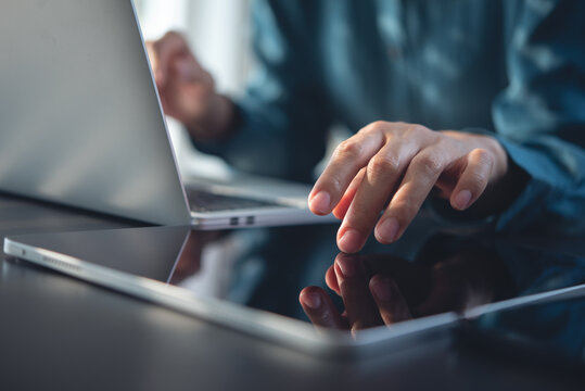 Closeup, woman using digital tablet, finger touching on screen with reflection during working on laptop computer on office desk. Internet technology, social media networking