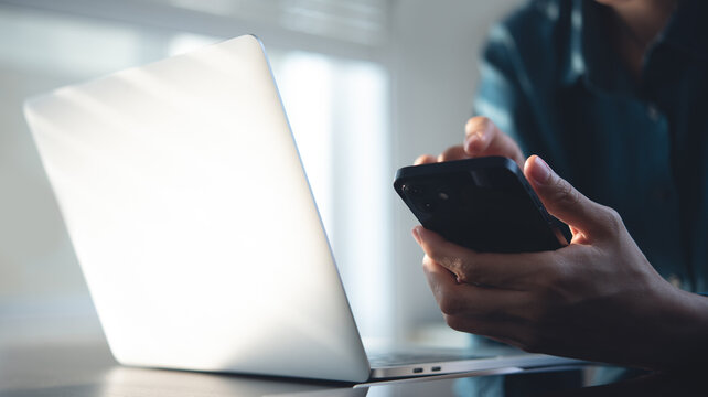 Woman using mobile phone during working on laptop computer at home office. Female using smartphone for online shopping, mobile banking and social networking