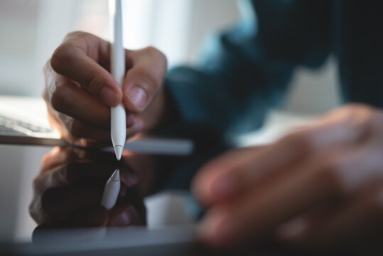 Close up, man hand with stylus pen signing on e-document via mobile release app on table office, electronic signature. Business man working on digital tablet, surfing the internet networking