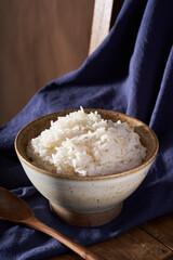 A close-up of a bowl of white rice against a blue fabric background.
