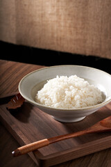 A close-up of a bowl of white rice against a vintage linen and wooden background.