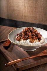A close-up of a bowl of Taiwanese braised pork rice against a retro linen and wooden background.