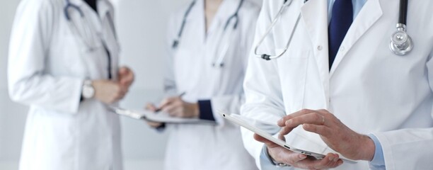 Doctors working together on medical records while a healthcare professional uses a digital tablet for patient data management in a technology-driven clinic