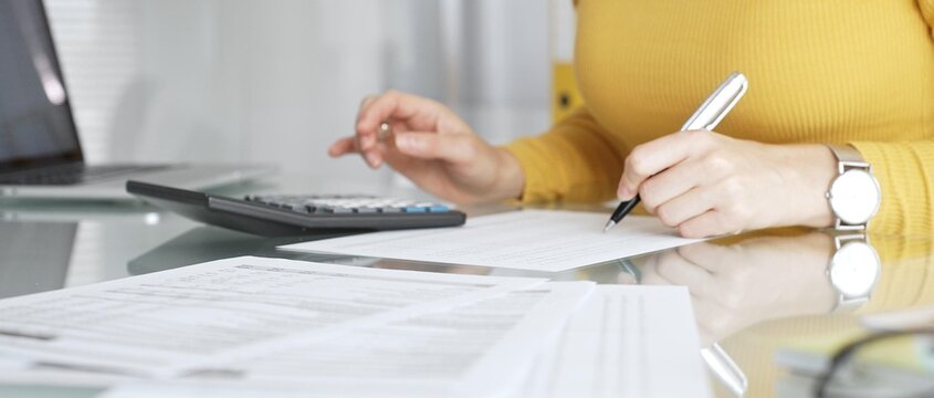 Woman calculating finance, taxes, and accounting paperwork at office desk, budgeting expenses, filing documents. Audit and taxes in business