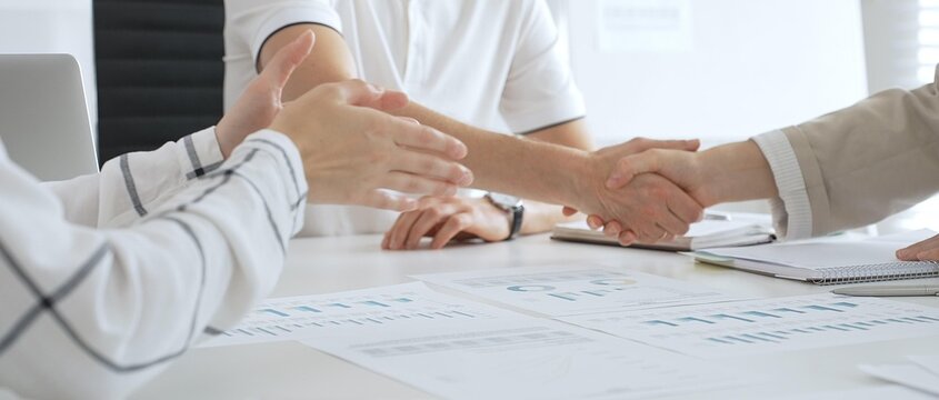 Businessman shaking hands with female partner over workplace documents, symbolizing collaborative spirit and shared workplace success. Business handshake concept