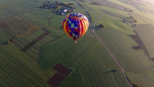 Vivid aerial imagery, Colorful balloon above rural scenery, Hot air balloon soaring over patchwork farmland during sunrise, Bright balloon drifting over countryside with scenic sunrise