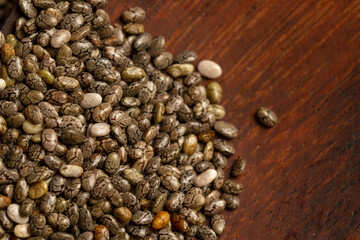 A top-down macro photograph captures a pile of dry chia seeds (Salvia hispanica) on a dark, textured wooden surface, with empty copy space to the right.