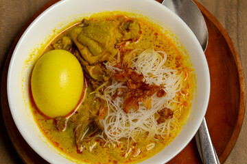 A close-up, top-down view of Bihun Kari from the Riau area, a Chinese-Indonesian fusion noodle soup. It consists of vermicelli, pieces of chicken, and a whole hard-boiled egg submerged