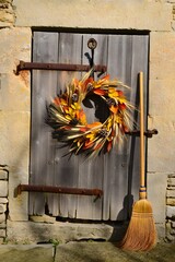 Fall wreath hanging on rustic wooden door with broom leaning against the wall outside