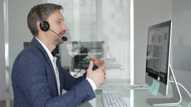 Man in headset talking during online video call, working in office, consulting remote customers, providing technical support. Business people concept