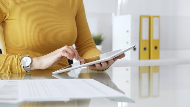 Woman freelancer working with digital tablet, browsing information, using online technology in modern office. Audit and taxes in business