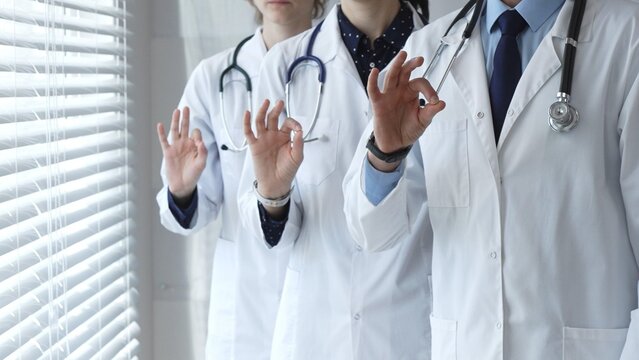 Medical team demonstrating professionalism and successful teamwork, doctors and healthcare workers in lab coats and stethoscopes showing ok sign for quality and well being
