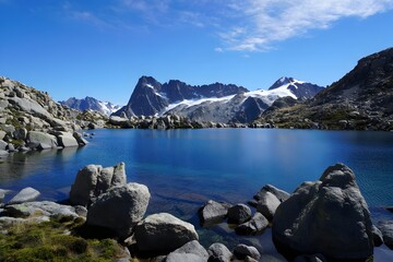 Mountain lake reflects the sky with snow capped peaks and rocky shorelines around it all