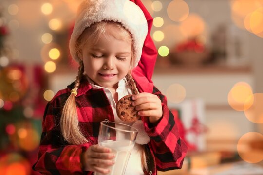 Cute little girl in Santa hat, with milk and cookie at home on Christmas eve